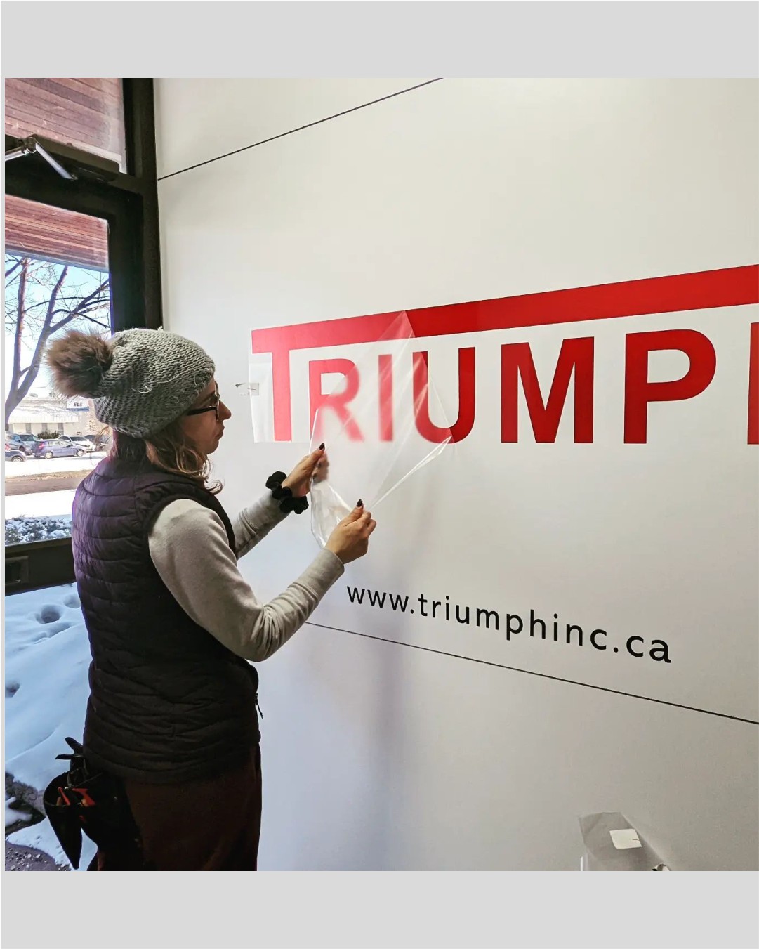 Professional installation of a large-format vinyl wall graphic for Triumph Inc. featuring red and black corporate branding.